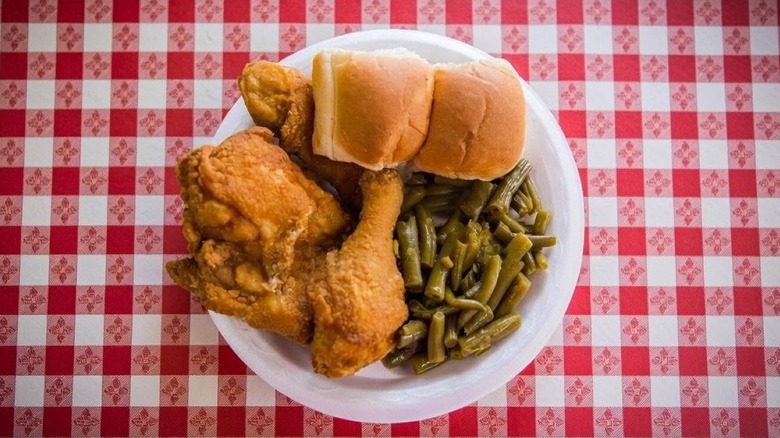 Top-down shot of plate of fried chicken, rolls, green beans, on red checkered tablecloth