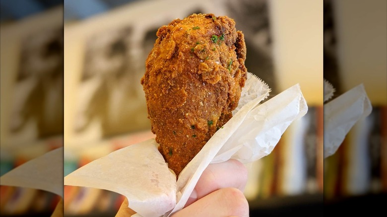 Hand holding crispy chicken leg in piece of waxed paper