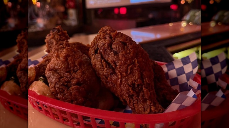 Dark crispy fried chicken in red basket on black and white checkered paper