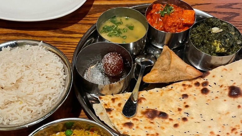 Bowl of rice alongside non-vegetarian thali with flatbread, samosa, and gulab jamun