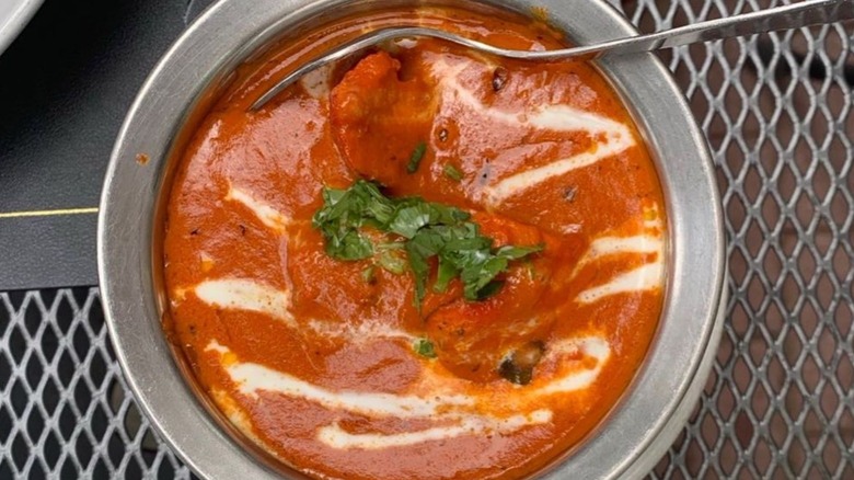 Chicken tikka masala garnished with cream and cilantro in serving bowl on outdoor table