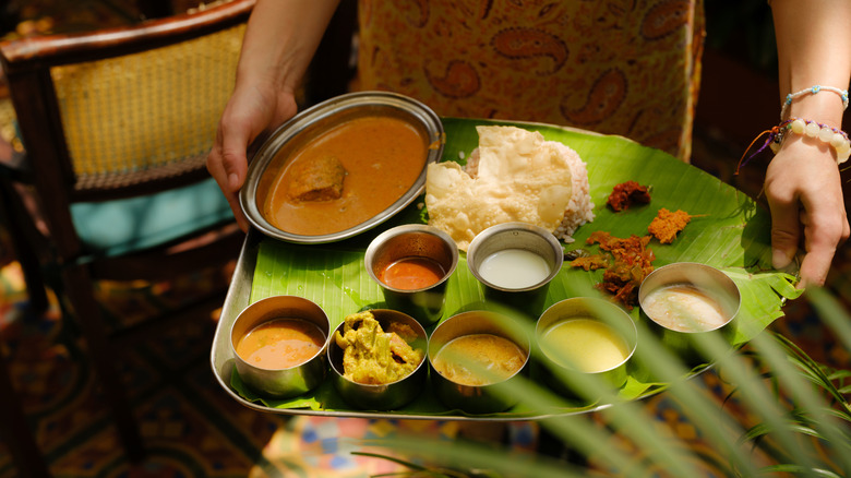 Woman holding tray with banana leaf, laden with South Indian specialties
