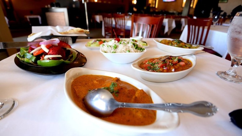 Several curries, salads, and bowl of rice on table laden with tablecloth
