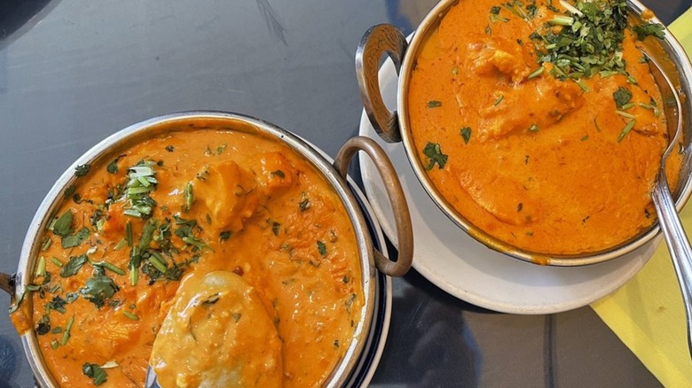 Two portions of butter chicken in serving bowls with spoons