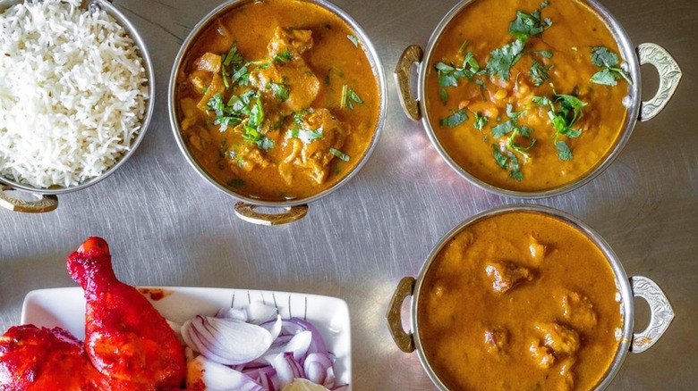 Overhead shot of chicken and several curries in elegant serving dishes alongside rice