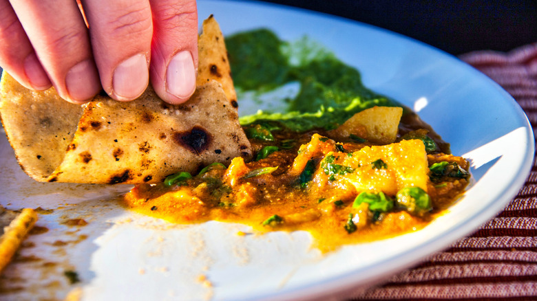 Hand using roti to eat sabzi from plate with chutney