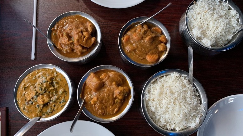 Two bowls of rice alongside aloo gobi, vegetable chettinadu, saag paneer, and chicken curry