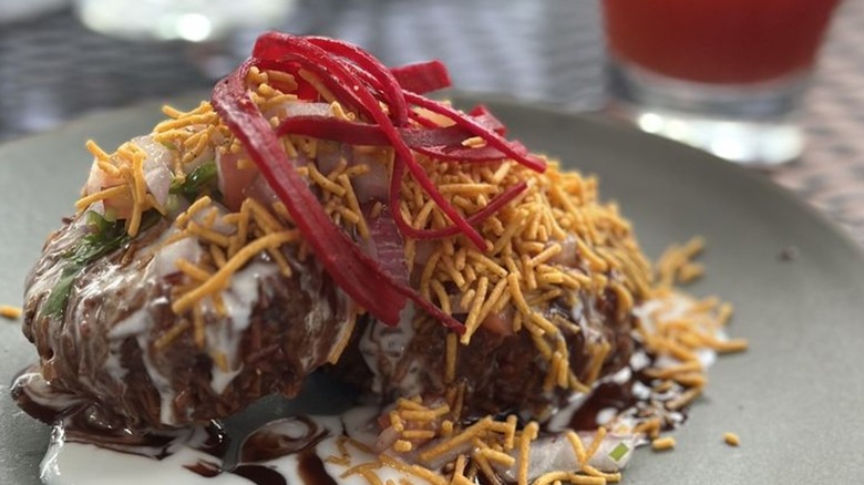 Beetroot tikki topped with tamarind chutney, sev, yogurt, and raw beetroot and onion