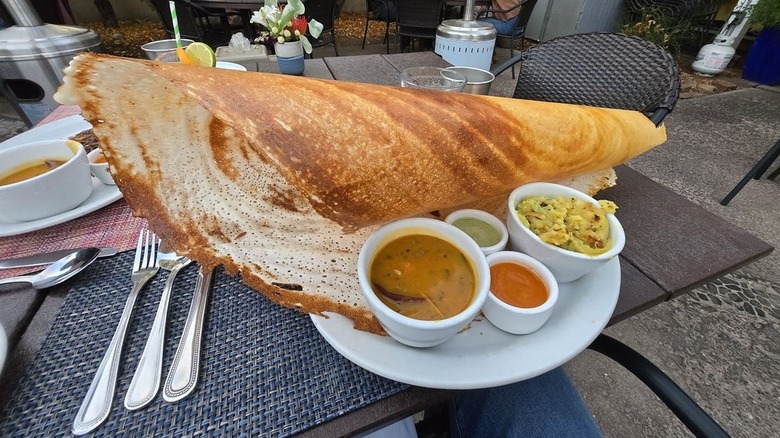 Large paper dosa on plate alongside sambar, potato masala, and two chutneys