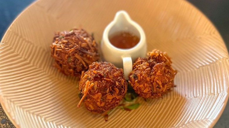 Three coconut prawn croquettes on plate alongside mirchi pani