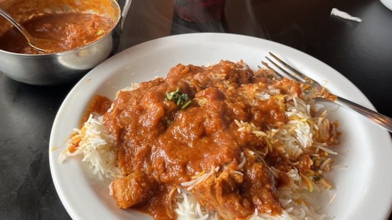 Plate of rice topped with chicken vindaloo, bowl full of curry in background