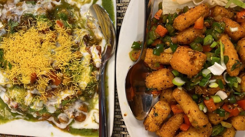 Overhead shot of chaat topped with sev, chutneys, and chickpeas, alongside plate of sauteed vegetables