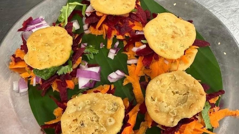 Chaat served on banana leaf with chopped onions and shaved carrots and beetroot