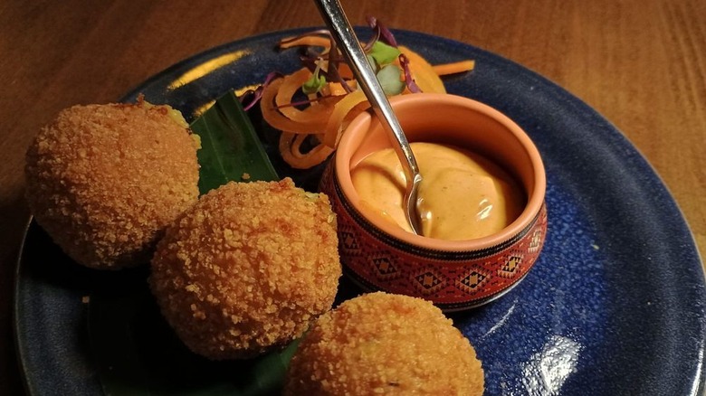 Three spring croquettes atop banana leaf on plate with sauce and raw vegetables