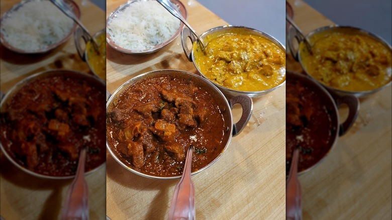 Bowl of rice alongside two curries in silver bowls on wooden table
