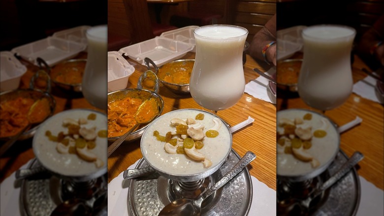 Rose lassi and kheer on table alongside two curries and takeout boxes