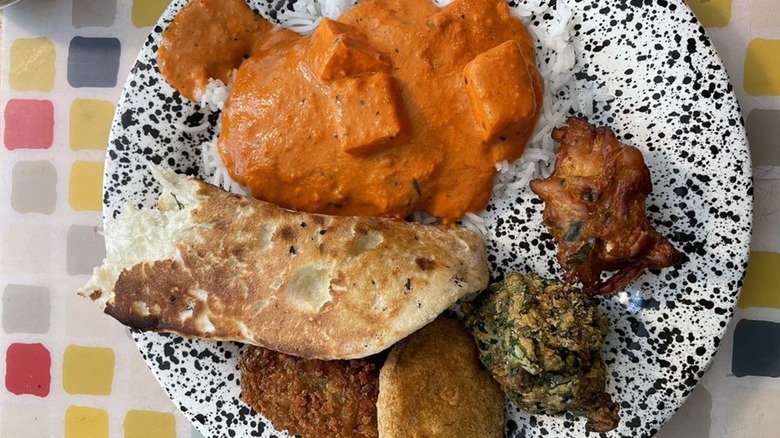 Plate laden with rice, vegetable cutlet, pakora, paneer butter masala, and garlic naan
