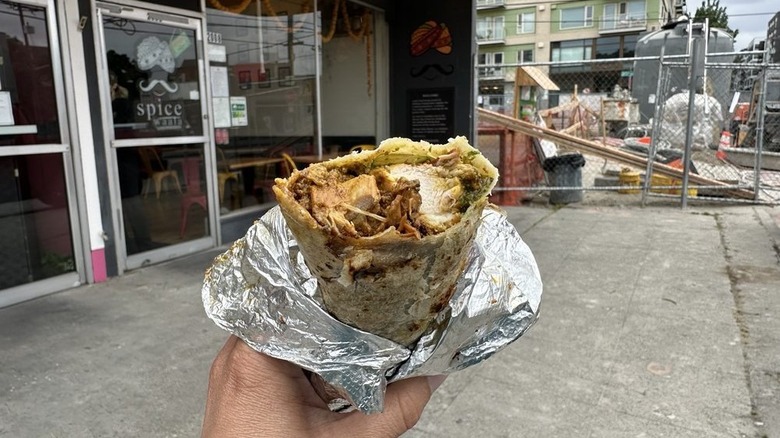 Hand holding chicken tikka kathi roll outside shop