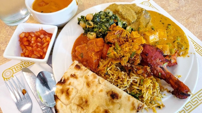Plate and bowls laden with buffet items, including rice, curries, meat, and naan