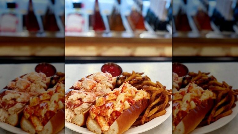 Two lobster rolls with fries and ketchup on white plate