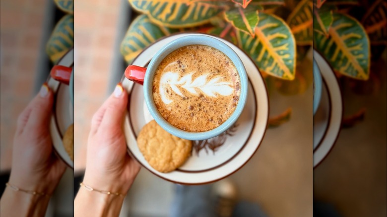 Hand holding saucer topped with mug of pumpkin spice latte and cookie