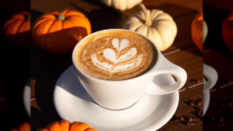 A pumpkin spice latte on wood table surrounded by small pumpkins.