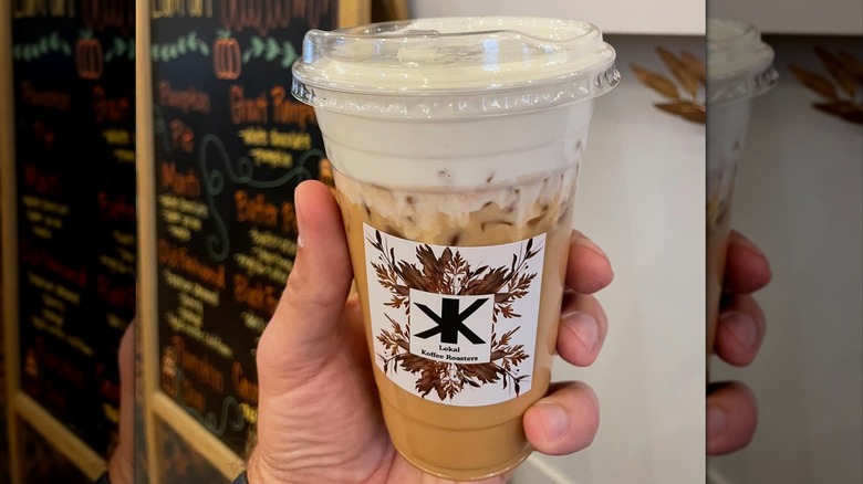 Hand holding iced pumpkin pie latte topped with maple cold foam in plastic to-go cup