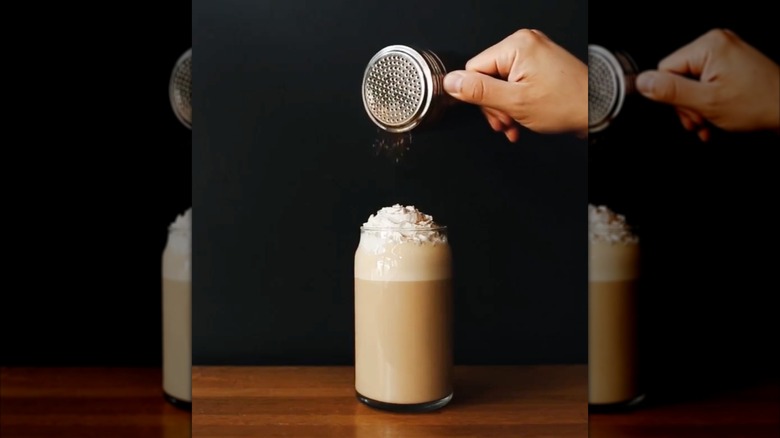 Hand sprinkling spices atop pumpkin spice latte in glass