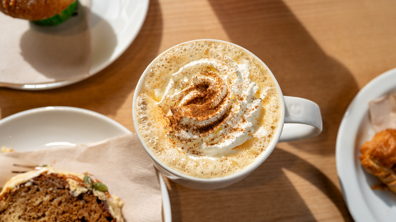 Overhead shot of pumpkin spice latte in mug, alongside various baked goods on table