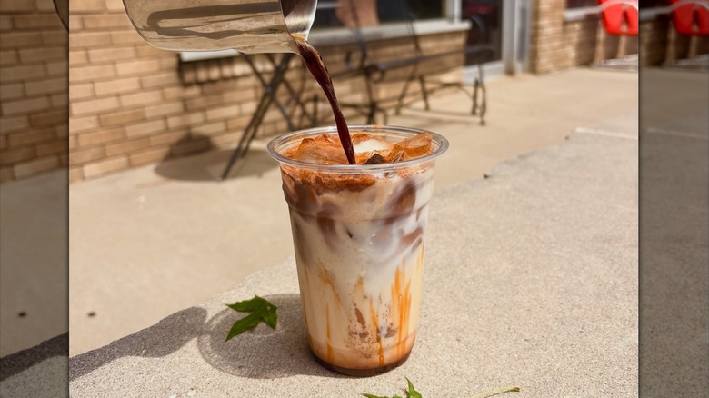 Coffee being poured into plastic cup of iced pumpkin spice latte