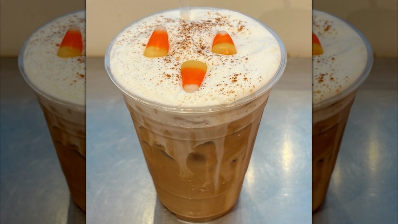 Pumpkin spice latte in plastic cup, topped with pumpkin cold foam and candy corn