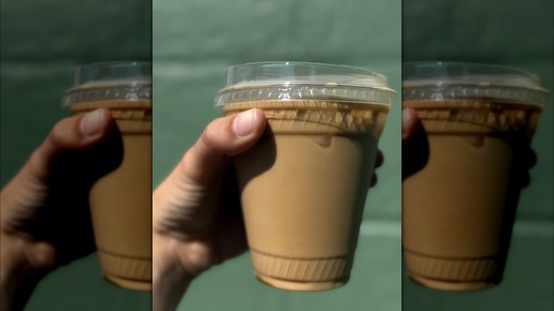 Hand holding pumpkin jam latte in plastic to-go cup