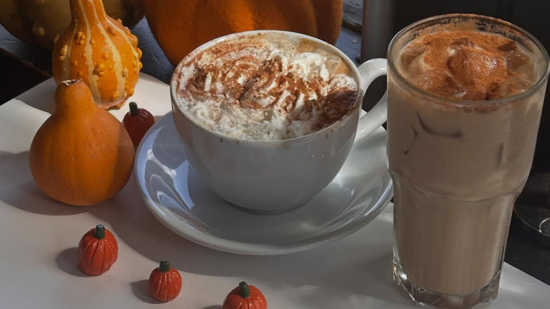 Hot and iced pumpkin spice latte on table alongside decorative gourds