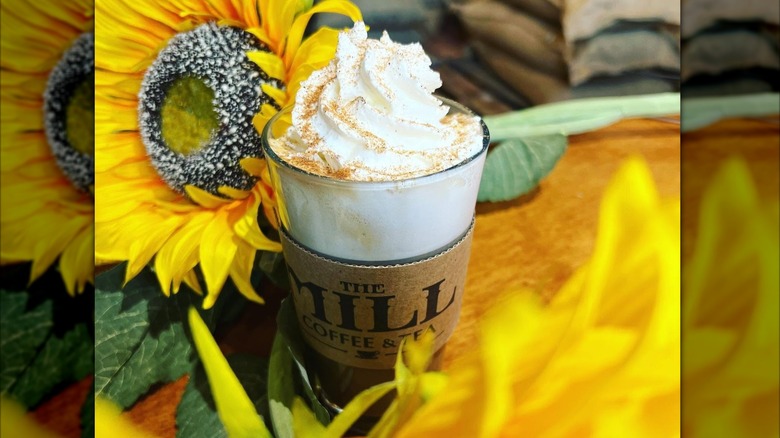 Pumpkin pie latte topped with whipped cream, set amidst sunflowers on table