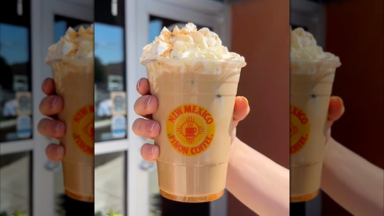 Hand holding iced pumpkin spice latte topped with whipped cream
