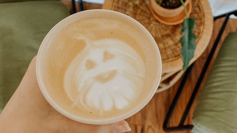 Overhead shot of hand holding pumpkin spice latte with pumpkin latte art