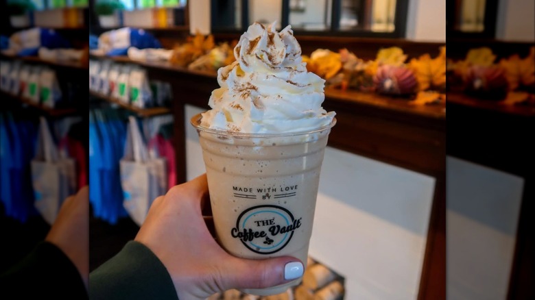 Hand holding frozen pumpkin spice latte topped with whipped cream