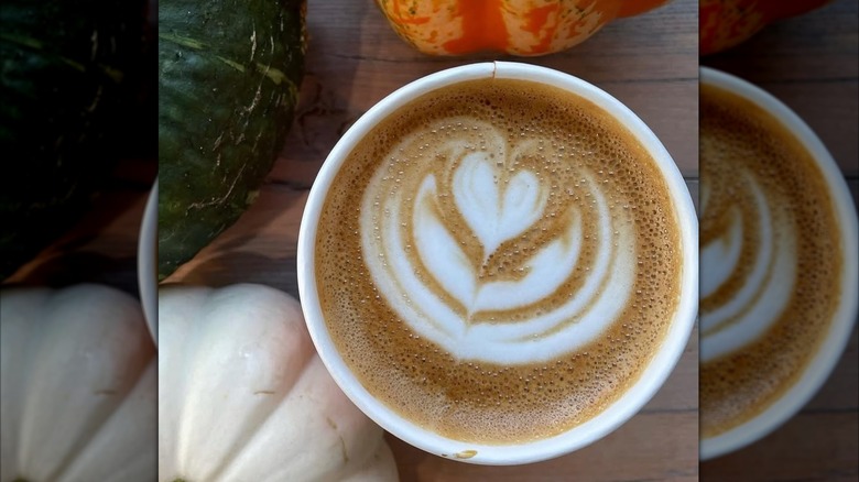 Overhead shot of pumpkin spice latte alongside pumpkins on table
