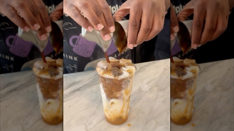Hands pouring two espresso shots into plastic to-go cup of pumpkin spice latte
