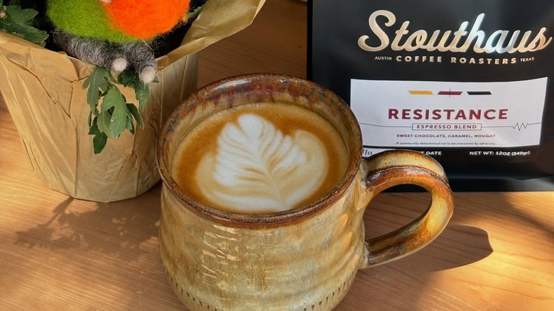Pumpkin spice latte in mug alongside bag of Stouthaus coffee and decorative felt plant