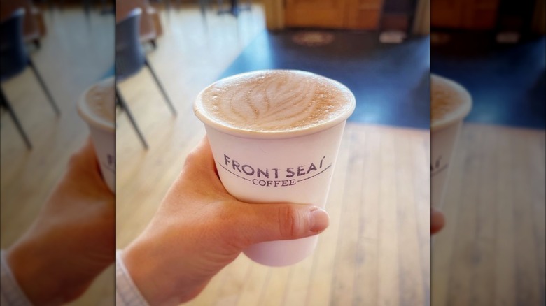 Hand holding pumpkin spice latte in to-go cup in shop