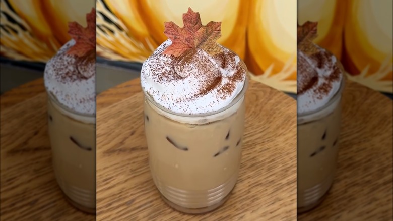 Iced pumpkin cookie butter latte topped with whipped cream, cinnamon, and decorative maple leaf