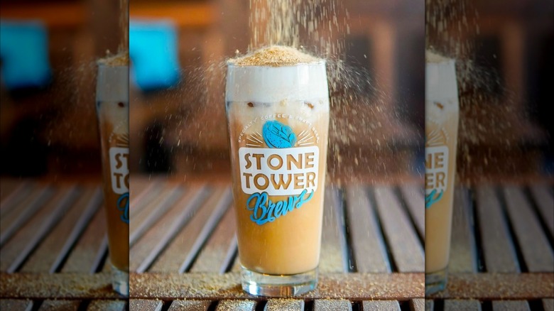 Iced Pumpkin Cheesecake Latte being sprinkled with sugary topping on wooden pallet