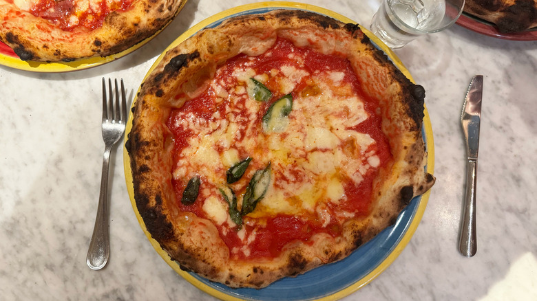 Margherita pizza from Concettina ai Tre Santi in Naples, Italy on white marble table, blue plate with yellow trim