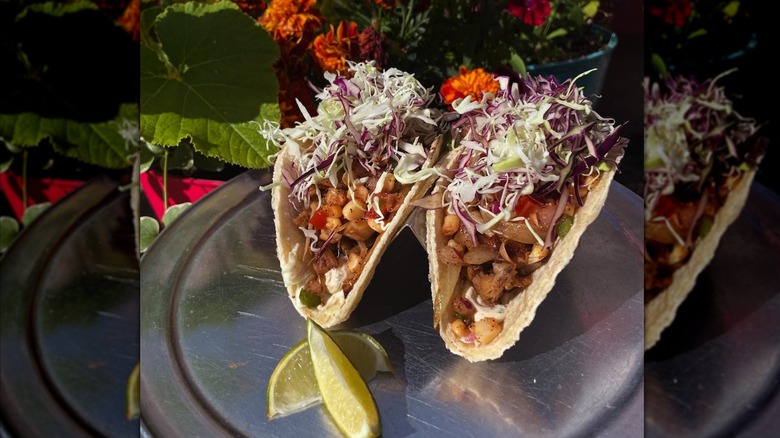 Two vegan jackfruit tacos and two lime wedges on a metal tray shot outdoors at El Green-Go's