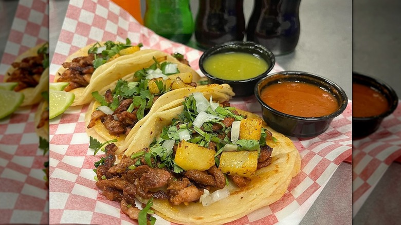 Three street tacos and sauce cups on red and white checked paper