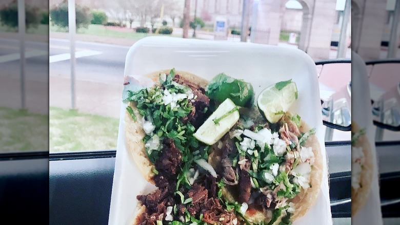 Hand holding styrofoam plate of street tacos with lime wedges in a car