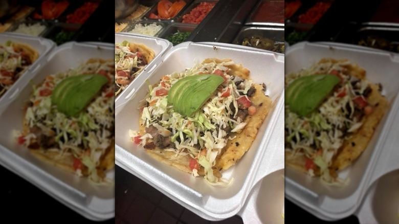 Large soft taco topped with avocado slices in styrofoam container