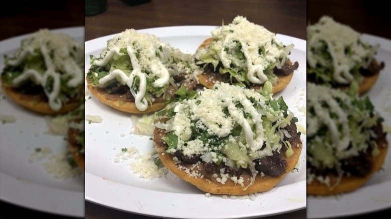 Three street tacos topped with lettuce and sour cream on plate