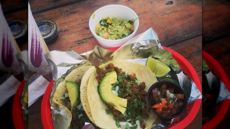 Tacos with avocado in red basket under styrofoam cup of guacamole